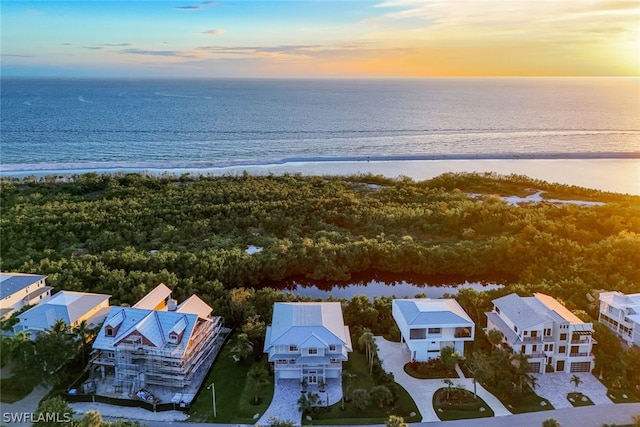 aerial view at dusk featuring a water view and a beach view