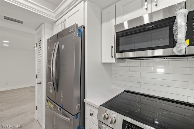 kitchen with decorative backsplash, ornamental molding, stainless steel appliances, and white cabinetry