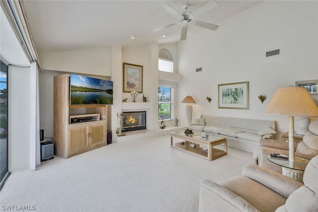 living room with a tiled fireplace, light colored carpet, high vaulted ceiling, and ceiling fan