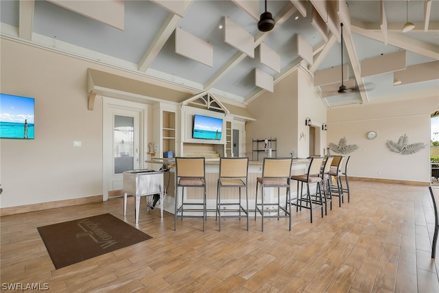 kitchen featuring beam ceiling, a breakfast bar, ceiling fan, light hardwood / wood-style floors, and high vaulted ceiling