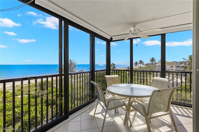 sunroom featuring ceiling fan, a water view, and a view of the beach