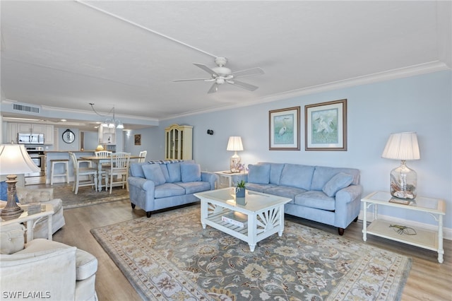 living room with wood-type flooring, ceiling fan with notable chandelier, and ornamental molding