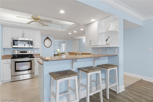 kitchen with kitchen peninsula, stainless steel appliances, ceiling fan, crown molding, and white cabinets