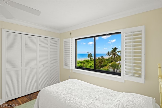 bedroom featuring dark wood-type flooring, a water view, crown molding, ceiling fan, and a closet