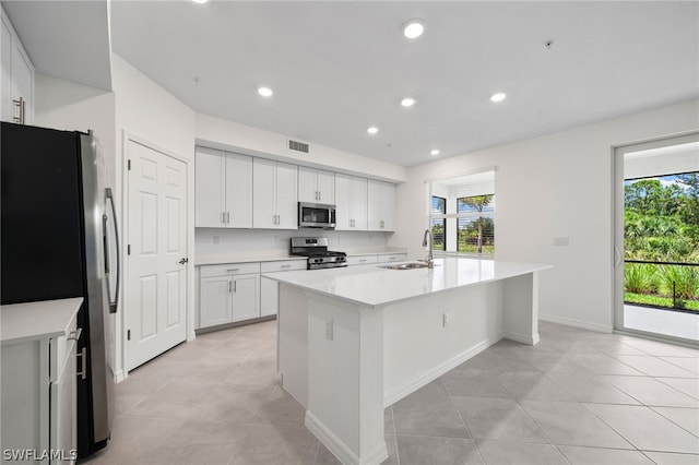 kitchen featuring sink, stainless steel appliances, light tile patterned floors, a center island with sink, and white cabinets