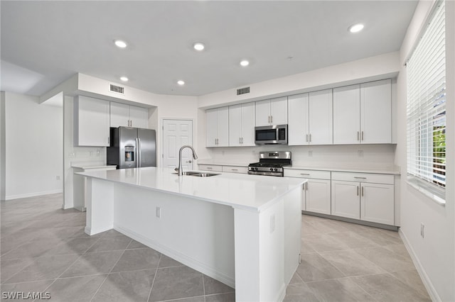 kitchen featuring sink, stainless steel appliances, light tile patterned floors, a center island with sink, and white cabinets