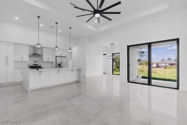 kitchen featuring a large island with sink, stainless steel appliances, white cabinets, wall chimney exhaust hood, and pendant lighting