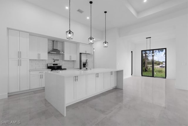 kitchen with wall chimney range hood, pendant lighting, appliances with stainless steel finishes, a spacious island, and white cabinetry