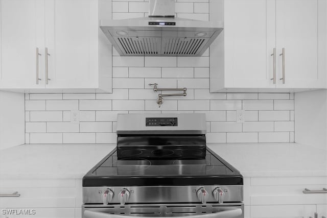 kitchen with wall chimney exhaust hood, backsplash, stainless steel stove, and white cabinets