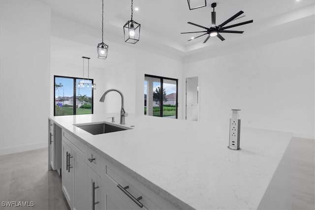 kitchen with an island with sink, light stone countertops, white cabinets, sink, and pendant lighting