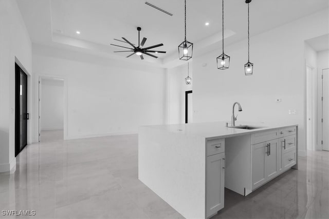 kitchen with an island with sink, decorative light fixtures, white cabinets, and a raised ceiling