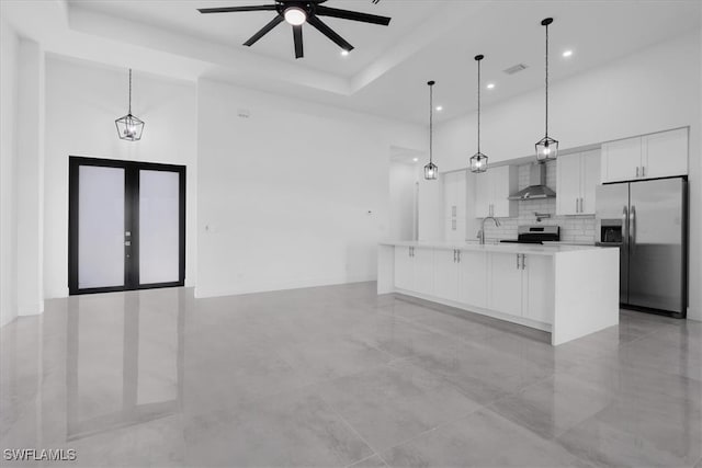 kitchen with white cabinets, hanging light fixtures, a large island, wall chimney exhaust hood, and appliances with stainless steel finishes