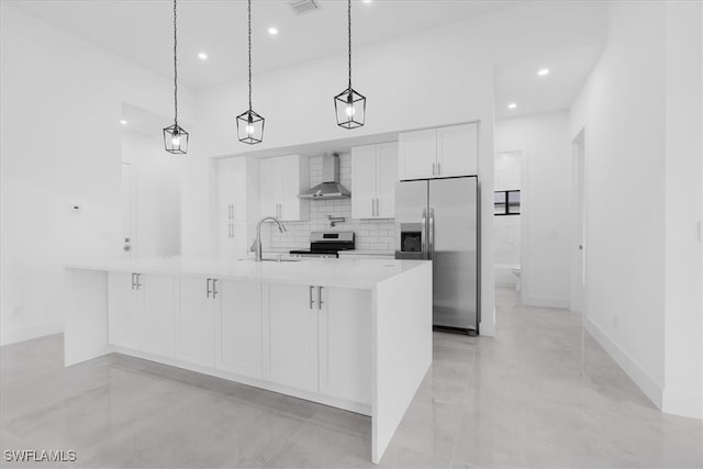 kitchen featuring stainless steel appliances, wall chimney exhaust hood, sink, hanging light fixtures, and white cabinetry