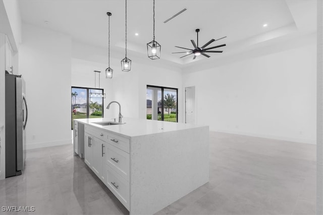 kitchen featuring pendant lighting, an island with sink, sink, white cabinetry, and stainless steel refrigerator