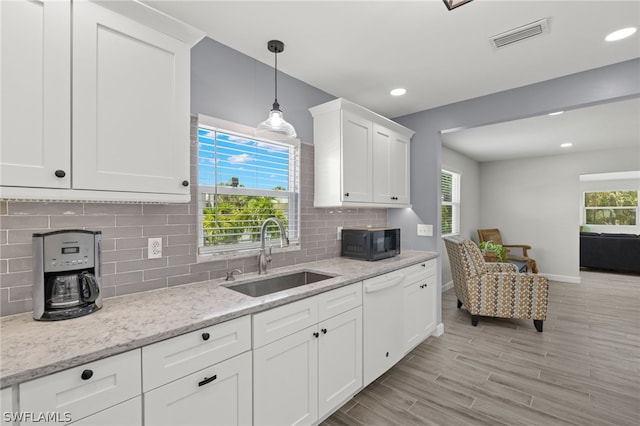 kitchen with pendant lighting, white dishwasher, sink, light stone counters, and white cabinetry