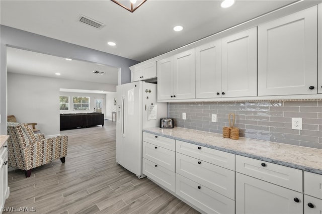 kitchen with white cabinets, white refrigerator with ice dispenser, tasteful backsplash, and light stone countertops