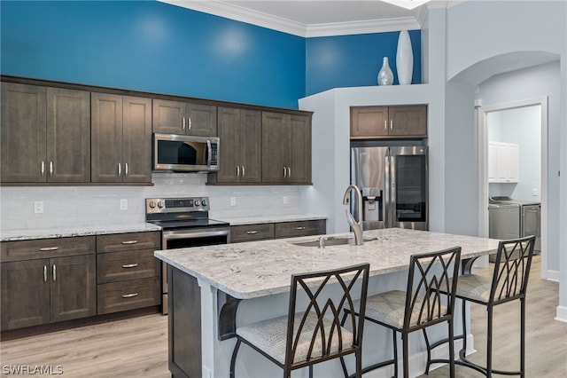 kitchen with sink, washing machine and dryer, an island with sink, dark brown cabinets, and stainless steel appliances