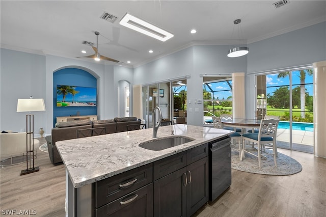 kitchen featuring sink, dishwasher, light stone counters, pendant lighting, and a kitchen island with sink