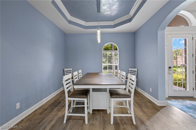 dining space with dark hardwood / wood-style flooring, a raised ceiling, and ornamental molding