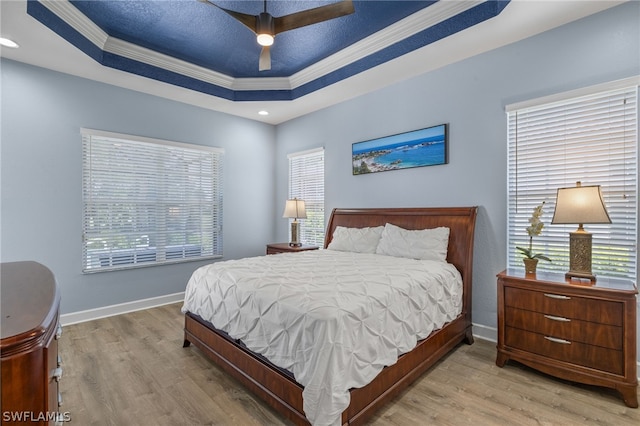 bedroom with light hardwood / wood-style flooring, a raised ceiling, ceiling fan, and crown molding