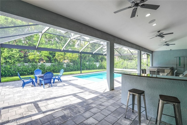 view of pool featuring glass enclosure, ceiling fan, a patio area, and a bar