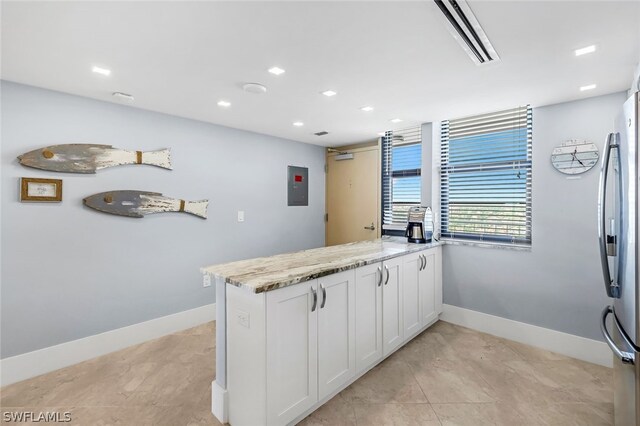 kitchen with kitchen peninsula, stainless steel fridge, light stone counters, light tile patterned floors, and white cabinetry