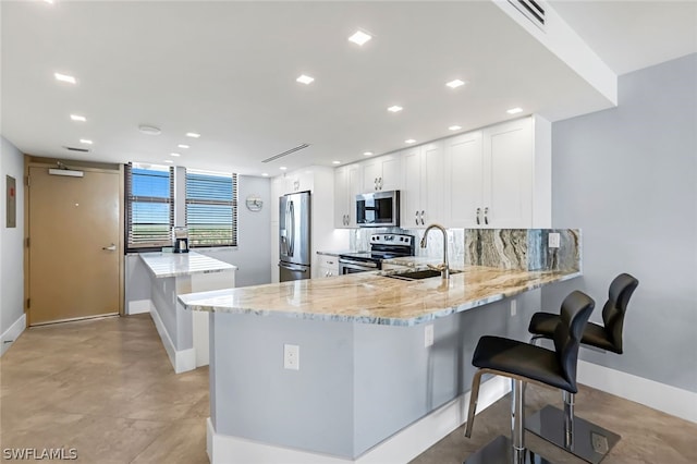 kitchen with white cabinetry, sink, stainless steel appliances, light stone counters, and kitchen peninsula