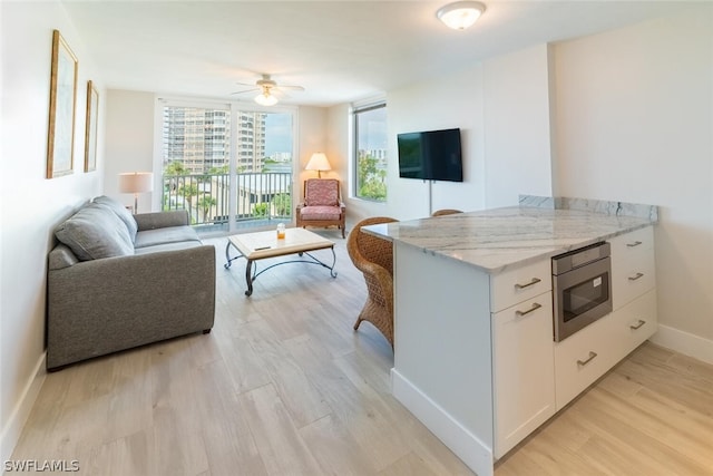 kitchen with light hardwood / wood-style flooring, light stone counters, floor to ceiling windows, stainless steel microwave, and white cabinets