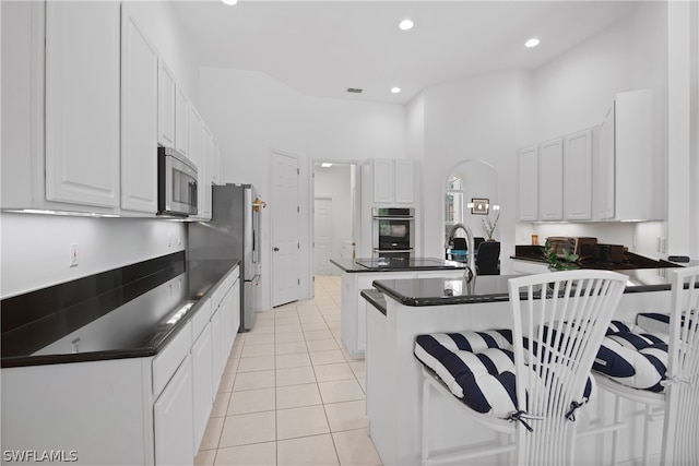 kitchen with appliances with stainless steel finishes, white cabinets, a breakfast bar area, and light tile patterned floors