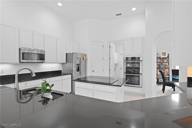 kitchen with white cabinetry, a towering ceiling, and appliances with stainless steel finishes