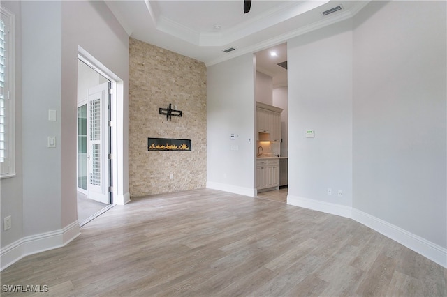 spare room featuring a fireplace, light wood-type flooring, a tray ceiling, ceiling fan, and ornamental molding