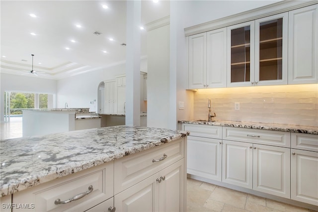 kitchen with backsplash, sink, ceiling fan, light stone counters, and white cabinets