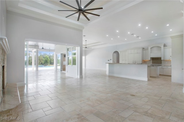 unfurnished living room featuring crown molding, a raised ceiling, a high ceiling, and ceiling fan