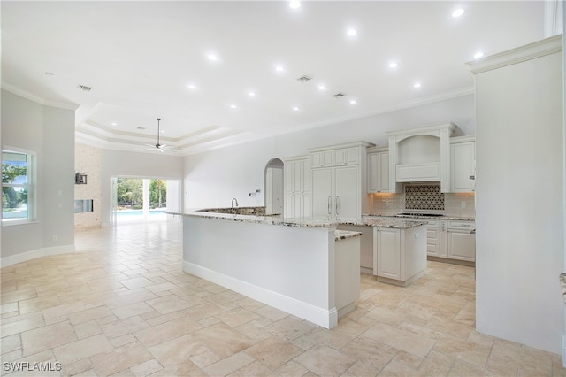 kitchen with a raised ceiling, gas cooktop, ceiling fan, light stone counters, and a large island