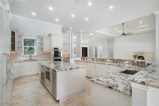 kitchen with stainless steel double oven, light stone counters, sink, a spacious island, and ceiling fan