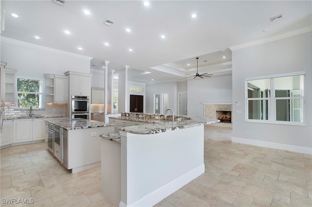 kitchen featuring a spacious island, white cabinets, ceiling fan, light stone counters, and double oven