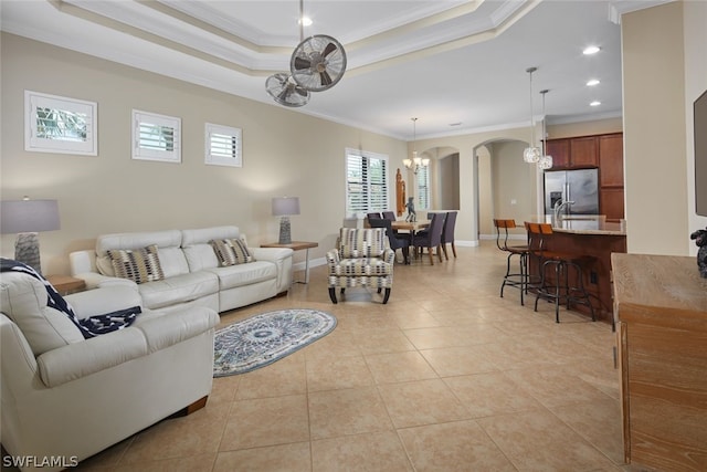 tiled living room featuring a raised ceiling, a notable chandelier, and ornamental molding