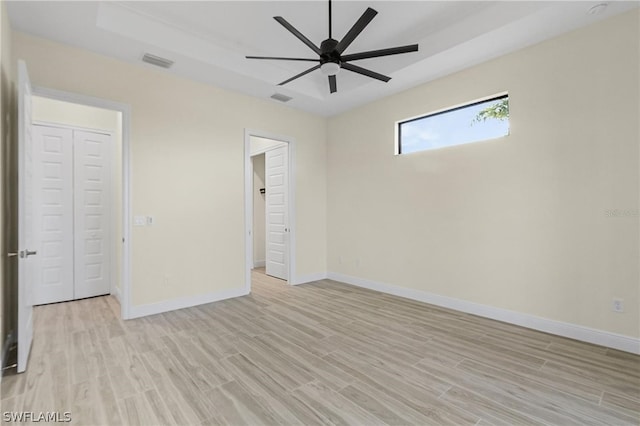 unfurnished bedroom featuring ceiling fan, a raised ceiling, and light hardwood / wood-style floors