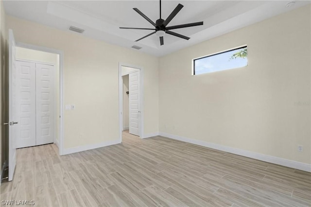 unfurnished bedroom with a raised ceiling, ceiling fan, and light hardwood / wood-style floors