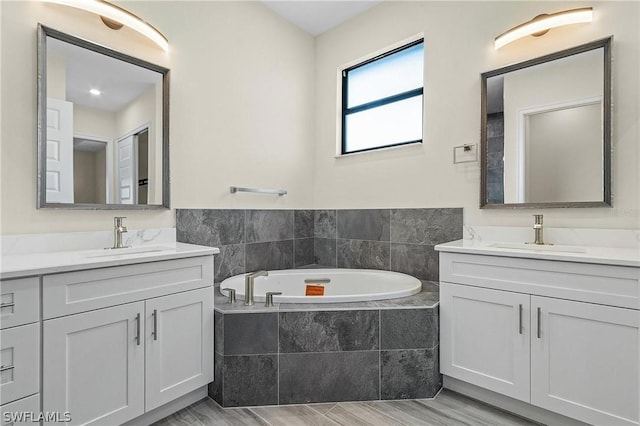 bathroom with a relaxing tiled tub, wood-type flooring, and dual bowl vanity