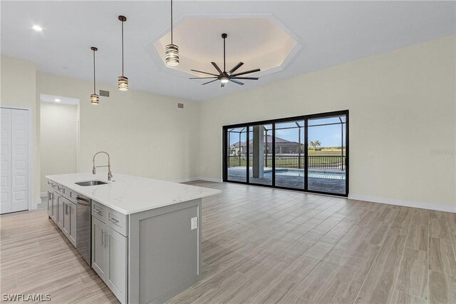 kitchen with ceiling fan, hanging light fixtures, sink, a center island with sink, and gray cabinetry