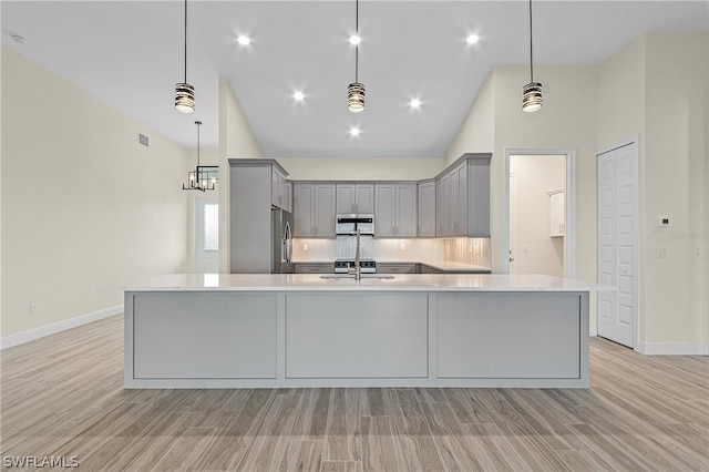 kitchen with tasteful backsplash, light hardwood / wood-style floors, appliances with stainless steel finishes, decorative light fixtures, and gray cabinetry