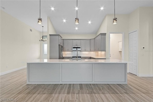 kitchen with gray cabinetry, hanging light fixtures, stainless steel refrigerator, and an island with sink