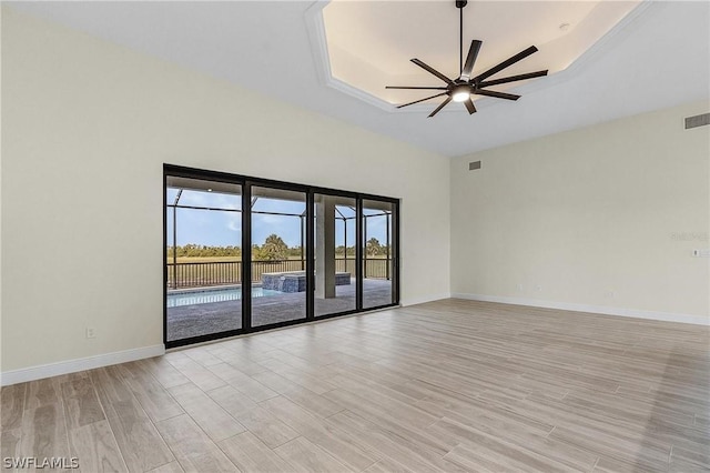 spare room featuring a raised ceiling, light wood-type flooring, and ceiling fan