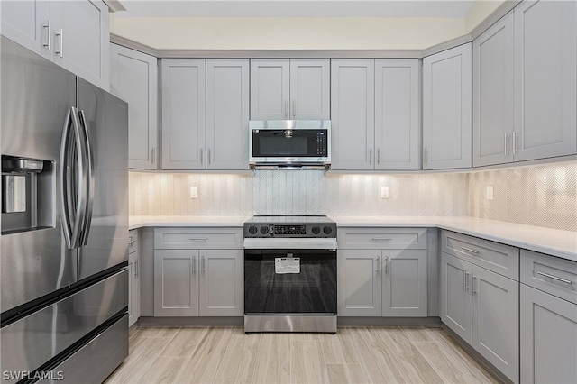 kitchen featuring gray cabinets, light hardwood / wood-style floors, decorative backsplash, and stainless steel appliances