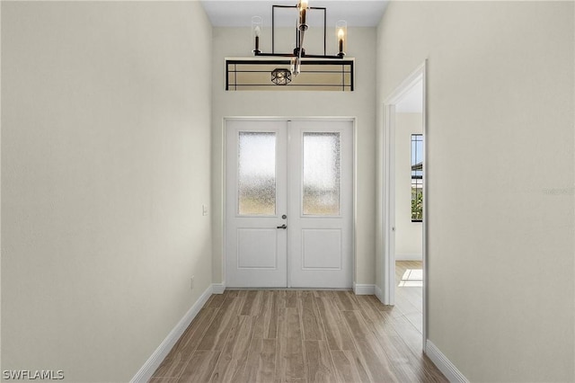 foyer with french doors, a healthy amount of sunlight, light hardwood / wood-style floors, and a notable chandelier