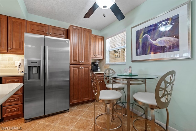 kitchen featuring light tile patterned flooring, backsplash, a textured ceiling, ceiling fan, and stainless steel fridge