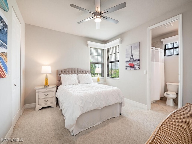 bedroom featuring ceiling fan, light colored carpet, ensuite bath, and multiple windows