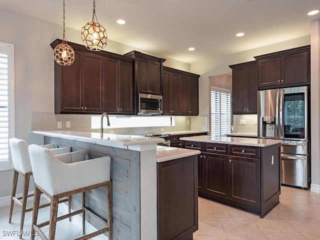 kitchen with pendant lighting, dark brown cabinets, a kitchen breakfast bar, stainless steel appliances, and kitchen peninsula