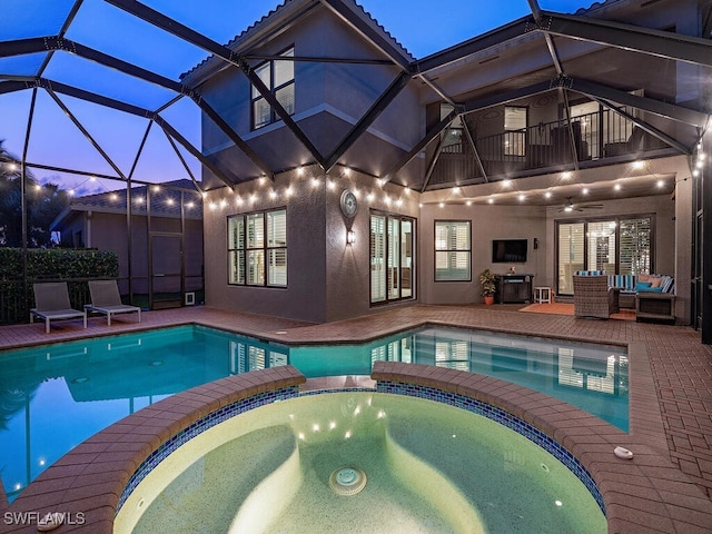 pool at dusk with a lanai, ceiling fan, an outdoor living space, a patio area, and an in ground hot tub